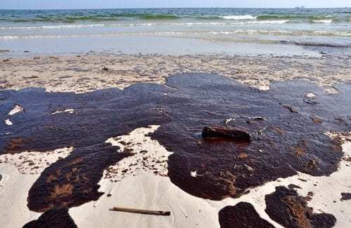 Oil spill on beach with off shore oil rig in background