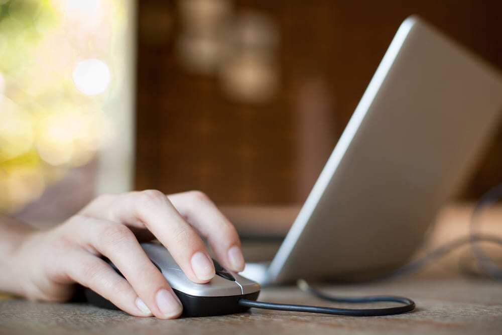 Close-up of female hand using mouse with laptop