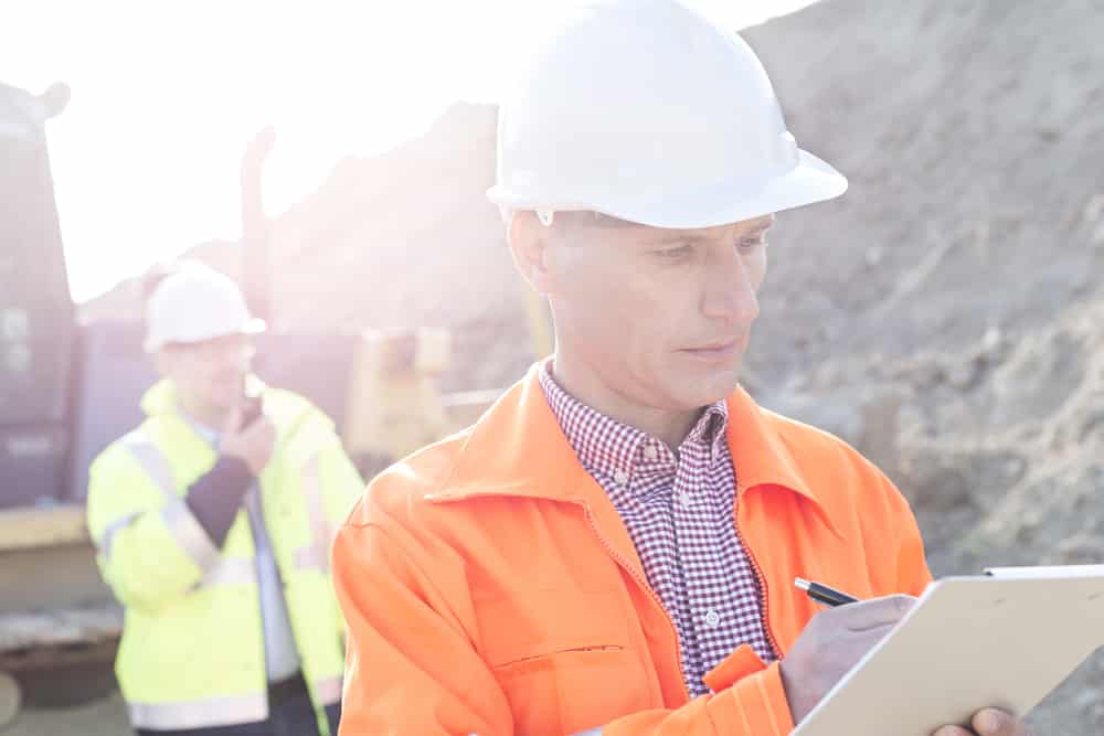 Man with hardhat using clipboard at outdoor site