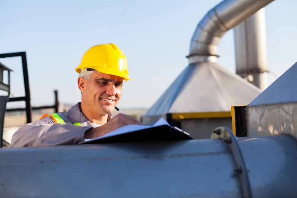 Man in construction hat in outdoor industrial environment writing on clipboard